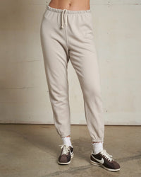 Someone wearing perfectwhitetee's Johnny French Terry Easy Sweatpant in Silver, paired with white socks and brown Nike sneakers, stands on a concrete floor against a plain light wall. The upper body is not shown.