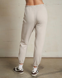 A person wears perfectwhitetee's Johnny French Terry Easy Sweatpant in Silver, paired with white socks and black-and-white Nike sneakers, standing on a concrete floor against an unfinished wall for relaxed loungewear vibes.