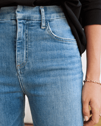 Close-up of a person wearing Frank & Eileen’s Derry Pant in 2001 Classic Blue Wash, paired with a black top. Their right hand, adorned with a gold bracelet, rests by the pocket of the premium Italian Dream Denim jeans.