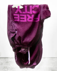 A pair of Free City Flap/Snap FC Large Matte/Satin Airjump Pants in Deeplove, featuring an elastic waist and bold "FREE CITY" lettering, folded neatly on a light textured surface.