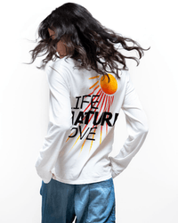 A person with long, wavy hair wears the Free City LNLSun Longsleeve T in Creamy Yum, which features a screen printed sun and rays with "LIFE NATURE LOVE" on the back, paired with blue jeans. The background is plain white.