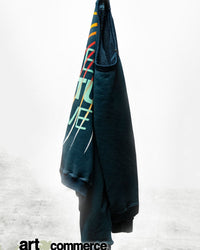 A dark green LNLSun Superyumm Biggie Raglan by Free City with colorful diagonal stripes and text hangs on a hook against a plain, light background. This oversized French lux terry pullover features a partial “art commerce” logo at the hem.