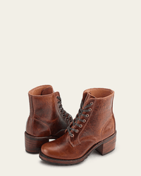 The FRYE Sabrina 6G Lace Up in Cognac boots, crafted from oil-tanned leather with stacked heels and a textured finish, are shown on a neutral background—one stands upright while the other leans to the side.