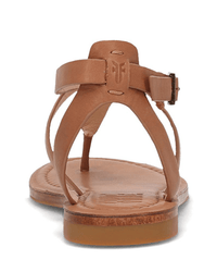 The FRYE Taylor Sandal in Tan features a minimalist design, slim adjustable ankle strap with side buckle, flat sole, visible stitching on the footbed, and full grain leather construction viewed from the back.