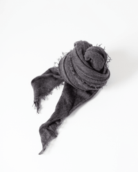 The Grisal Love Cashmere Scarf in Black Coffee is rolled into a spiral with its frayed ends elegantly trailing on a white background.