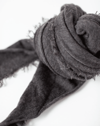 A close-up of the Grisal Love Cashmere Scarf in Black Coffee, featuring soft, textured cashmere fabric with frayed edges, loosely rolled and displayed against a white background.