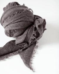 A close-up of the Grisal Love Cashmere Scarf in Brown Top, featuring a textured luxury knit with frayed edges, loosely knotted against a white background.