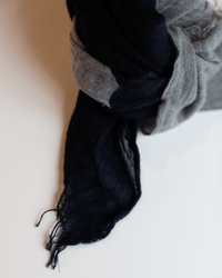A close-up of the Grisal Love Duo Mini scarf in Navy & Hthr Grey, softly tied with frayed ends, resting on a light surface.