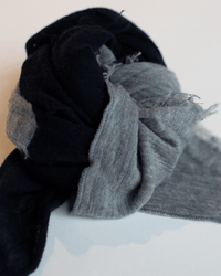 A close-up of the Grisal Love Duo Mini scarf in Navy & Hthr Grey, loosely knotted to highlight its frayed edges and soft texture, set against a plain white background.