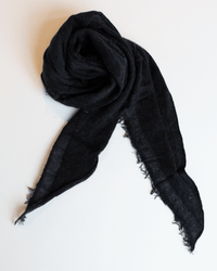 The Grisal Love Mini in Black X Charcoal, featuring frayed edges, is displayed on a white surface, loosely folded in a spiral with its ends extending outward.