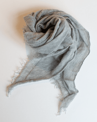 The Grisal Love Mini in Hthr Grey X Milk is a soft, ribbed cashmere scarf with fringed edges, loosely rolled and displayed on a white surface to highlight its delicate texture and light gray color.
