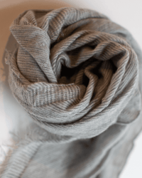 A close-up of Grisal’s Love Mini in Hthr Grey X Milk rolled into a spiral, highlighting its soft folds, textured fabric, and fringed edges.