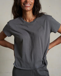 A woman smiles with her hands on her hips, wearing the Harley Cotton S/S Boxy Crew Tee in Charcoal by perfectwhitetee and matching pants against a neutral background.