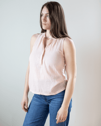 A woman with long brown hair, wearing the Hartford Tulette Henley Tank in Blush and blue jeans, stands against a plain light background, gazing slightly to the side with a neutral expression.