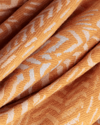 Close-up of folded pastel orange fabric from the Scarf / Etole 70 3D Hedwige by Inoui Editions, showing a white chevron pattern. Its cotton-wool blend reveals a soft, textured weave and fine craftsmanship.