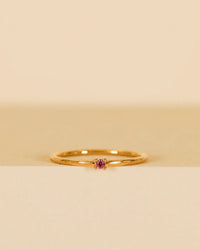 The JaxKelly Pinky Ring - Pink features a delicate design with a central cubic zirconia gemstone, showcased on a neutral beige and off-white background.