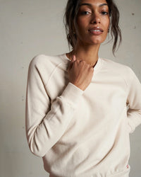 A woman wears the perfectwhitetee Alexi French Terry Sweatshirt in Sugar, standing against a plain background with a relaxed expression and one hand touching her collar.