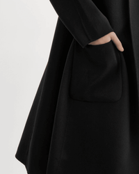 A person wearing the Lamarque Thara Jacket in Black, featuring oversized sleeves and a large front pocket with their right hand inside, is set against a plain white background.