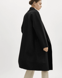A woman with her hair in a bun wears the Lamarque Thara Jacket in Black, featuring oversized sleeves, over light-colored pants against a plain white background.