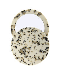 The Circle Mirror in Terrazzo by Machete features a round, compact design with a cream, black, and tan speckled cover, shown open to reveal the mirror inside.
