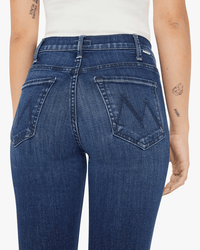 A person wears Mother’s Lil Hustler Ankle in Heirloom jeans, featuring ankle length and dark blue wash with “M” stitched back pockets, paired with a white sleeveless top; tattoos are visible on their left arm.