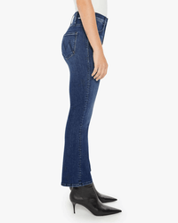 A person stands in profile wearing the Mother Lil Hustler Ankle in Heirloom petite high-rise flare jeans and black pointed-toe heeled boots against a plain white background.