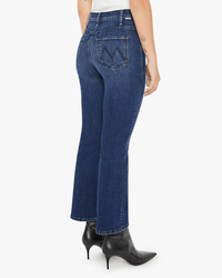 A person wearing Mother’s Lil Hustler Ankle in Heirloom dark blue petite high rise flare jeans and black heeled boots, shown from the back. The ankle length jeans feature back pocket stitching and a slim, slightly flared fit.