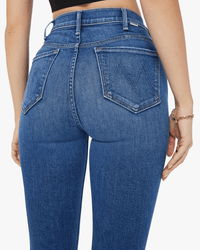 A person wearing Mother's The Hustler Ankle Fray in Grasping At Straws high-waisted blue jeans and a black crop top, shown from the back with visible stitching and large back pockets.