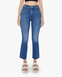 Someone wears Mother The Hustler Ankle Fray in Grasping At Straws jeans, a black crop top, and white sandals while standing against a plain white background.