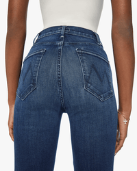 A person wearing Mother’s The Hustler Ankle in Heirloom—a vintage-wash high-rise flare jean with M-stitched back pockets—paired with a white top. Only the back view from waist to mid-thigh is visible.