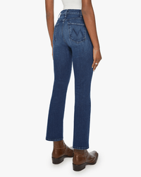 Someone wearing Mother’s The Hustler Ankle in Heirloom—a high-rise flare jean with back pockets—and brown ankle boots stands facing away; the vintage-inspired jeans feature a slightly flared leg.