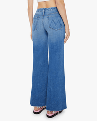 A person wearing the Mother The Roller Fray in Work Hard Play Hard jeans with a faded wash, raw hem, and back pockets, facing away from the camera. Styled with sandals and a sleeveless top.