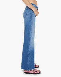 A person stands in profile wearing Mother’s The Roller Fray in Work Hard Play Hard jeans with a raw hem and pink embellished sandals, focusing on the lower body against a plain white background.