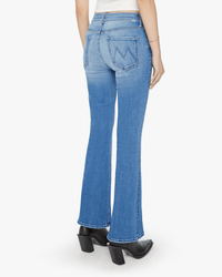 A person shown from the back wears Mother’s The Weekender in Layover light wash, mid-rise flare jeans with stitched back pockets, paired with black heeled boots and a white top.