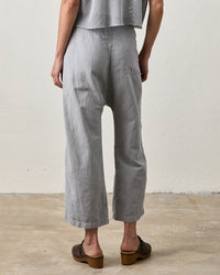 A person stands indoors on a concrete floor, facing away from the camera, wearing NSF's Akari Tie Waist Pants in Pale Grey, a gray textured top, and brown platform sandals.