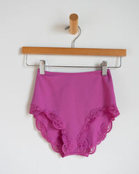 The Only Hearts Del w/ Lace High Cut Brief in Wild Rose, featuring delicate lace details, hangs from a wooden hanger against a plain white wall.