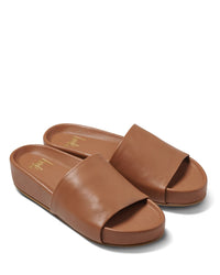 The beek.. Pelican in Tan are chic brown leather slide sandals with open toes, flat soles, and a cushioned memory foam footbed, shown on a white background.