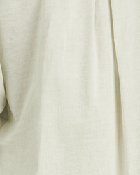 Close-up of the Jess Blouse Hushed Meadow in Verde Micro Stripe by Trovata Birds of Paradis, showcasing its beige, lightly textured fabric with subtle vertical lines and gentle folds.