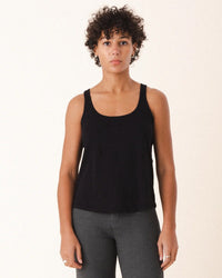 A person with short curly hair wears the Prairie Underground Layering Racerback Tank in Black and dark gray pants, standing facing forward against a plain light background.