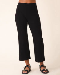 Someone wearing Prairie Underground's Rib Knack in Black pants and black sandals with buckles stands against a neutral background.