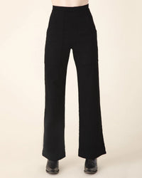 A person models the Prairie Underground Yr Arrow Pant in Black—high-waisted, wide-leg pants with seam details and front pockets—against a plain light background, showing only their lower torso and legs.
