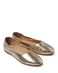 The beek. Swiftlet in Gold is a pair of metallic gold leather ballet flats with a rounded toe, light brown interior and sole, and molded arch support, shown against a white background.
