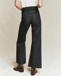 A person stands with their back to the camera, wearing the Great’s The Dock Jean in Rinse Wash—dark blue wide leg sailor jeans—styled with a white short-sleeve shirt and brown ankle boots against a neutral background.
