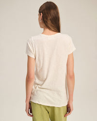 A person with straight brown hair is seen from behind, wearing the Tilly Short Sleeve Crew Neck Top in Coconut by Velvet by Graham & Spencer and light green pants against a plain background.