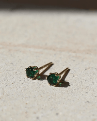 The May Birthstone Studs in 14K Gold Fill by Token Jewelry, featuring round deep green gemstones, are displayed on a textured light surface under bright natural light.