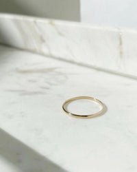 The Minimal Midi Ring by Token Jewelry, crafted in thin 14k gold fill, rests on white marble in soft natural light, highlighting its handmade simplicity and elegant design.