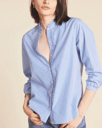Wearing the Trovata Birds of Paradis Helena Shirt in Blue/White Stripe with top buttons undone and sleeves rolled up, paired with blue jeans, a person stands against a neutral background.
