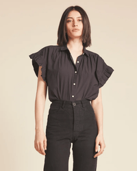 Wearing the Marianne B in Black by Trovata Birds of Paradis, a person with straight, shoulder-length dark hair stands against a plain beige background.