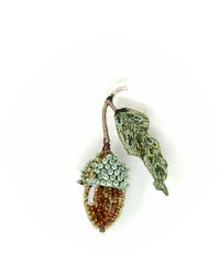 The Trovelore Acorn Brooch Pin features a brown beaded nut, light blue beaded cap, and green embroidered leaf, all handmade and displayed against a plain white background.
