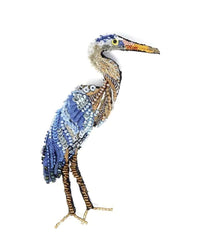A heron is illustrated with colored buttons and beads in blue, white, brown, and orange tones—resembling the Trovelore Blue Heron Brooch Pin—arranged to form the bird’s body and beak on a white background.